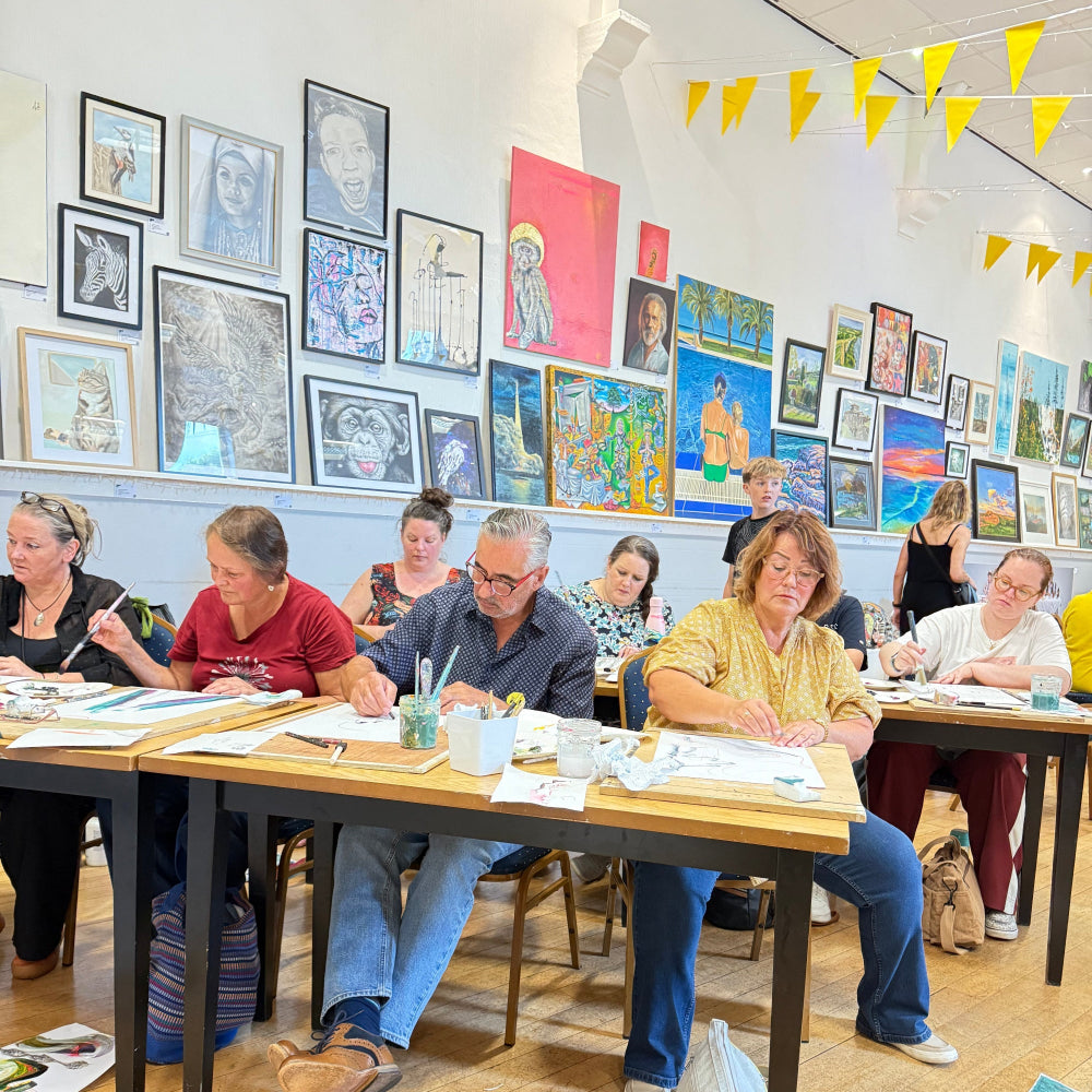 People gathered around a table with various framed artworks on a wooden floor.