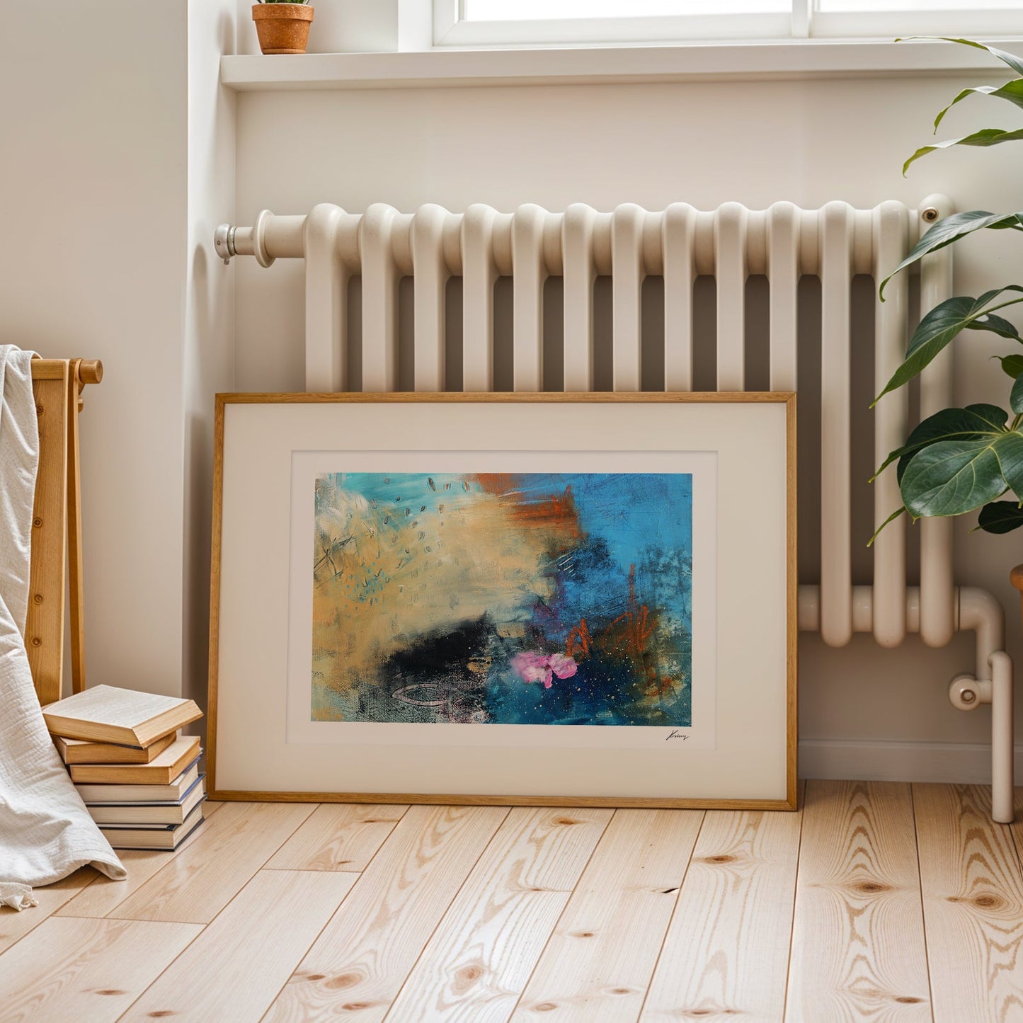 Framed abstract painting on a wooden floor with a radiator and plant in the background