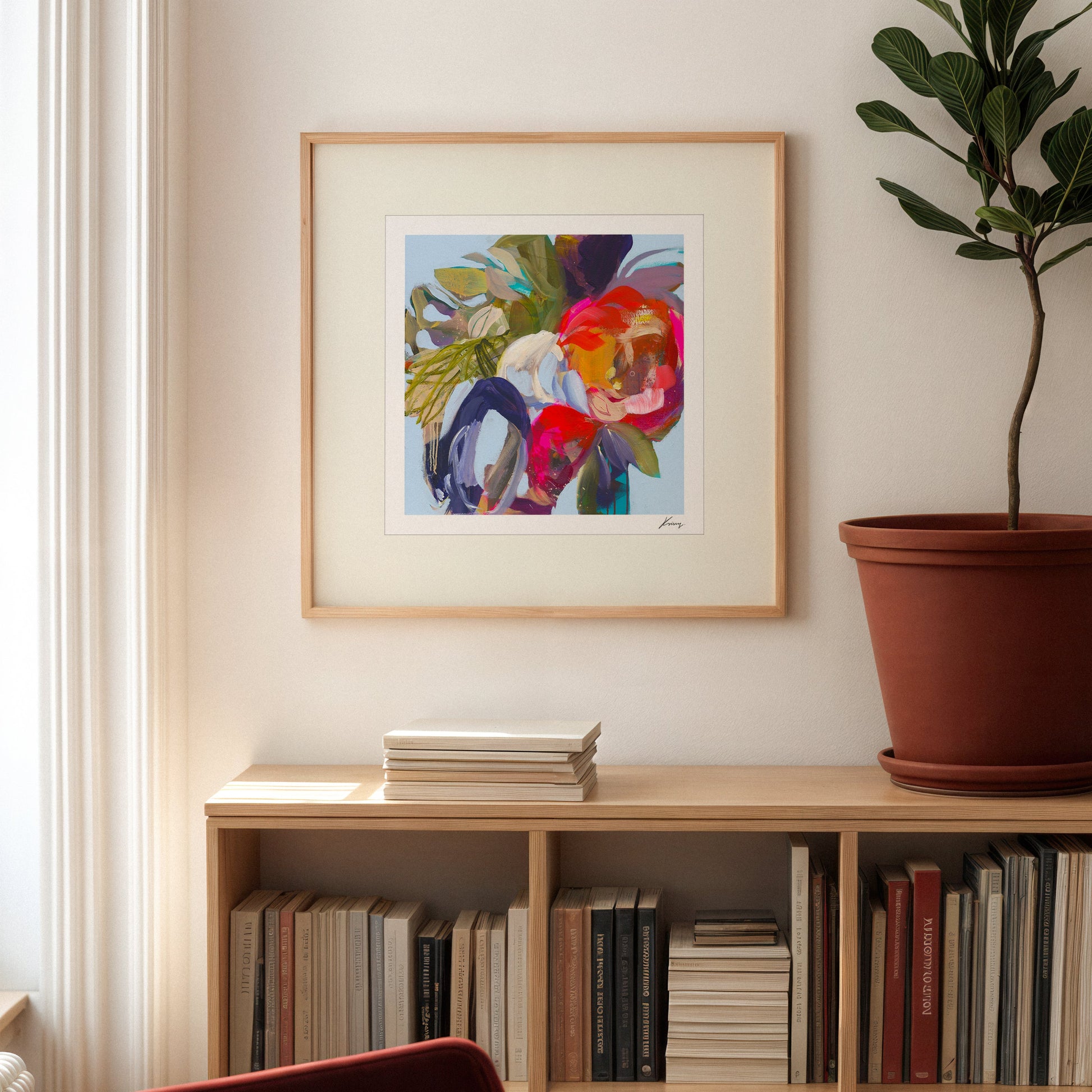 Framed abstract artwork on a wall above a bookshelf with books and a plant.