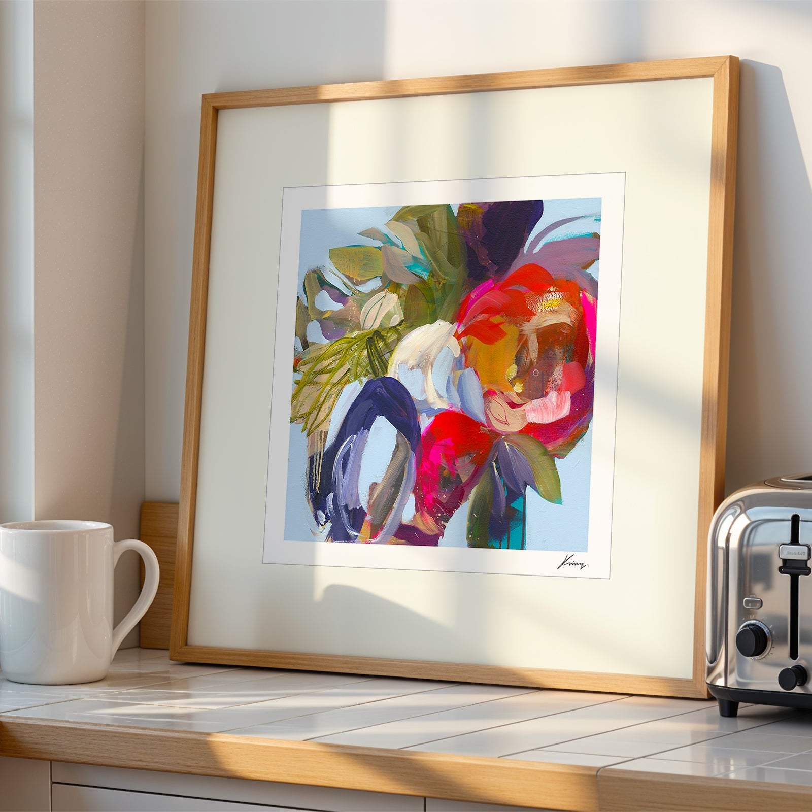 Framed colorful abstract art on a kitchen counter with a mug and toaster.