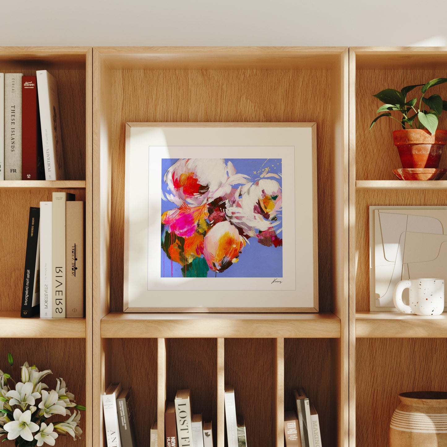 Framed floral artwork on a wooden bookshelf with books and decor items.