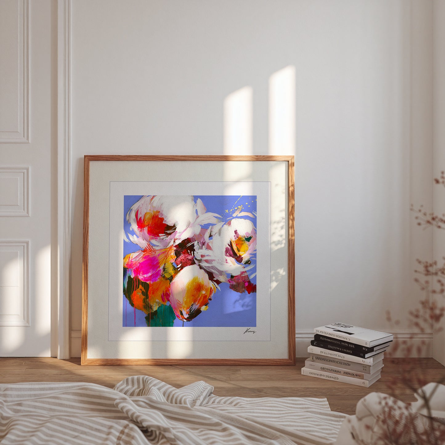 Framed abstract artwork on a wall with books and a blanket on a wooden floor.