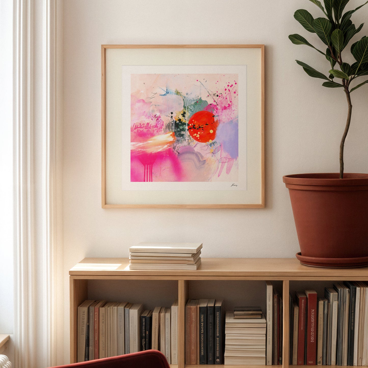 Framed abstract art on a wall above a bookshelf with books and a plant.