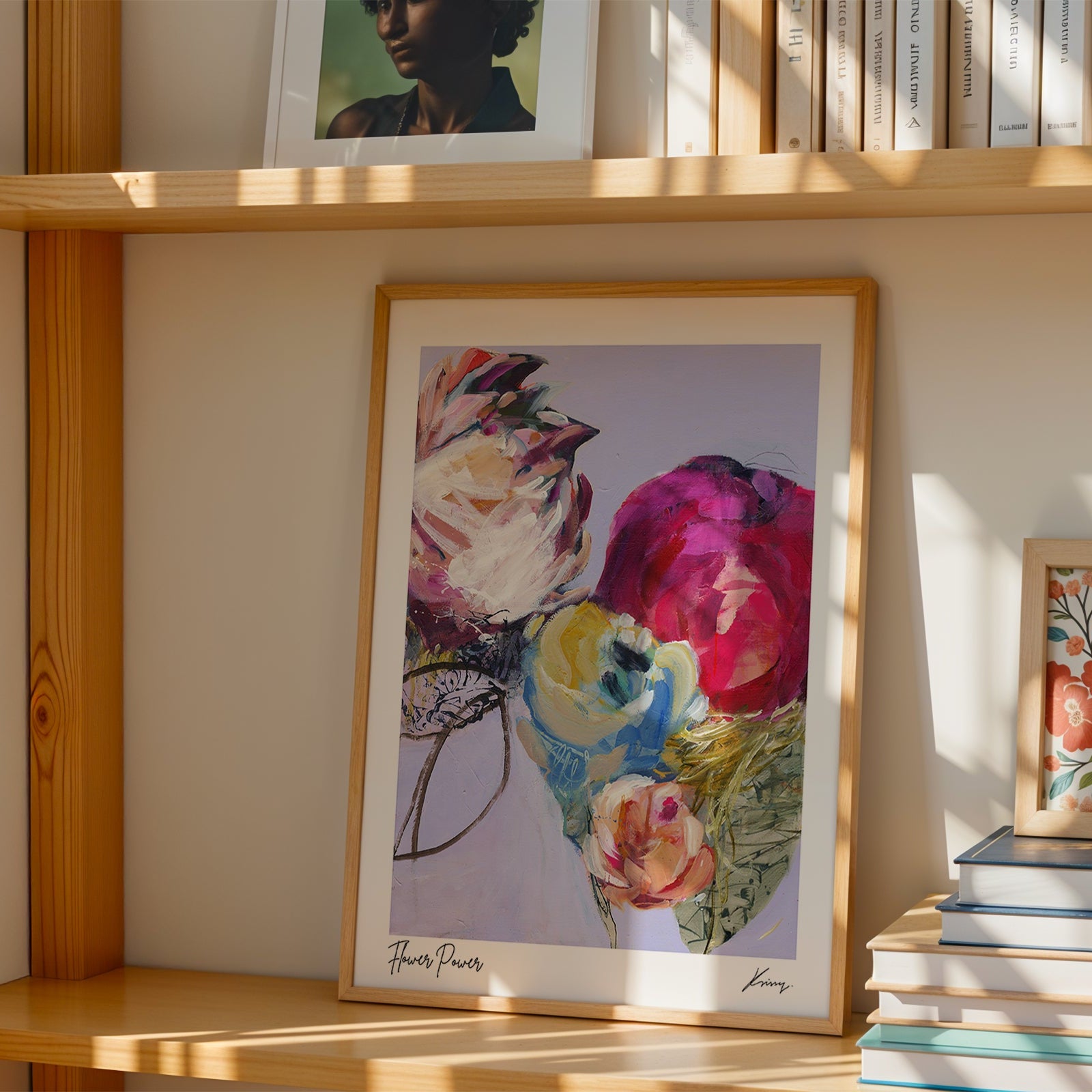 Framed floral artwork on a wooden shelf with books and another framed picture.