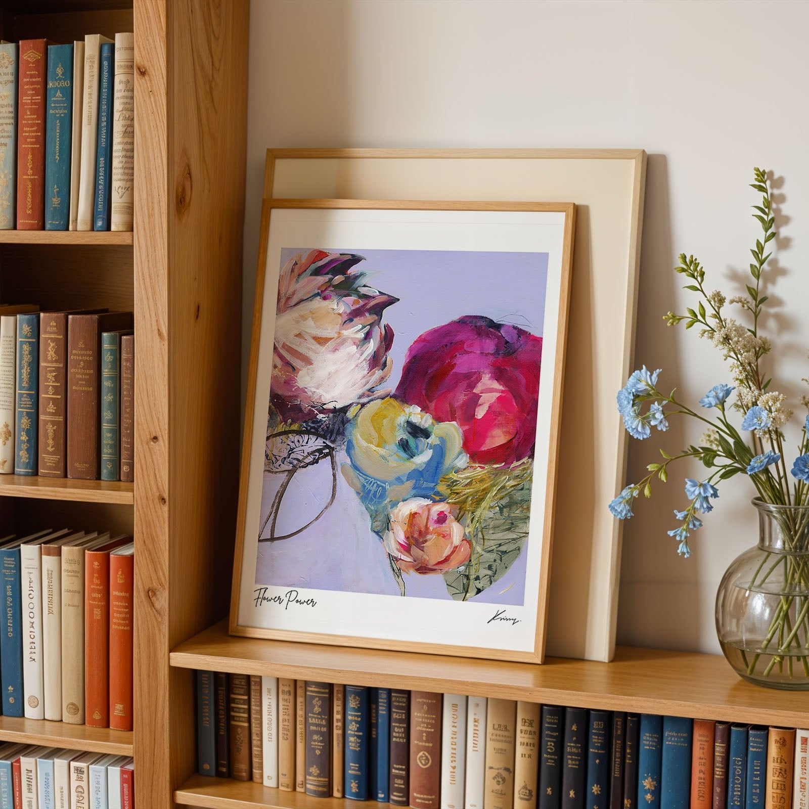 Framed floral print on a bookshelf with books and a vase of flowers.