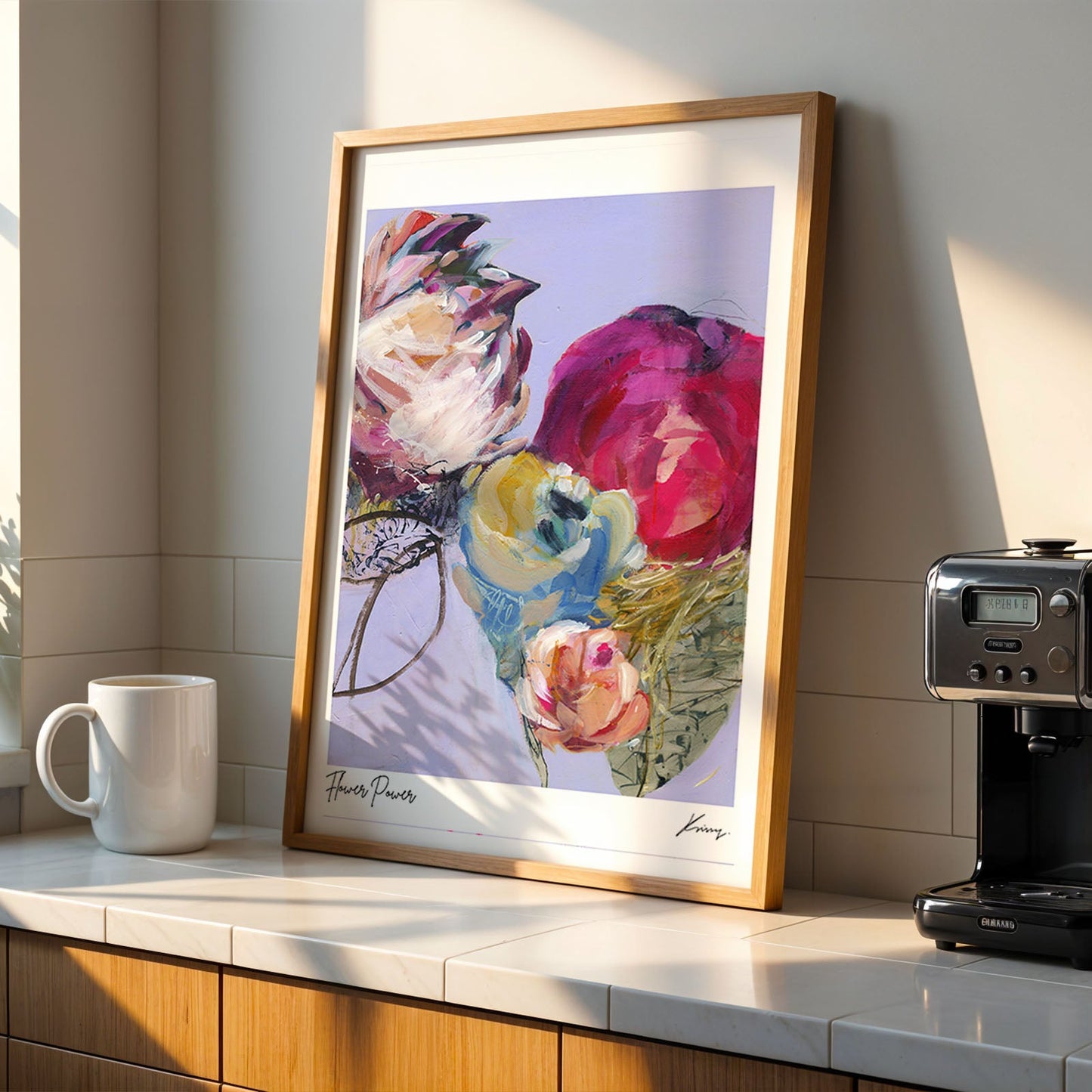 Framed floral art on a kitchen counter with a coffee machine and mug.