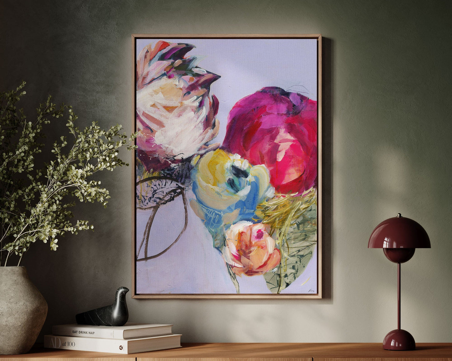 Colorful floral painting on a wall above a wooden console table with books and a lamp.