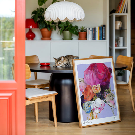 Dining room with a framed floral painting on a table, surrounded by chairs and decor.