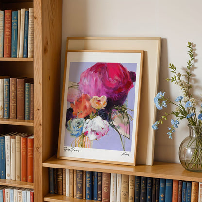 Framed floral art on a bookshelf with books and a vase of flowers.