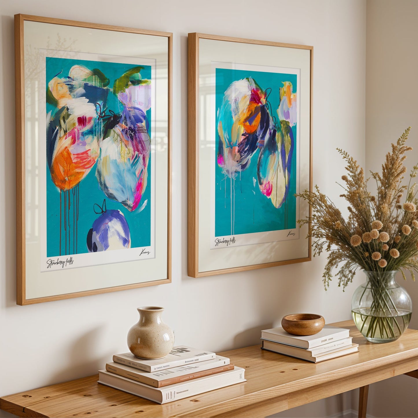 Two abstract art pieces on a wall above a wooden console table with decorative items.