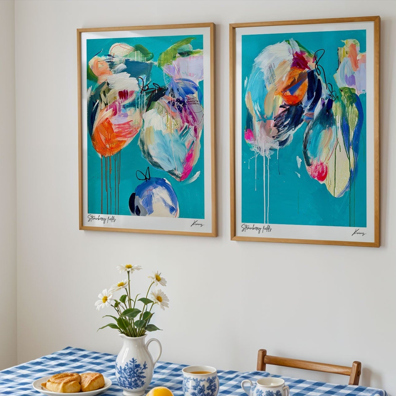 Two abstract art pieces on a wall above a table with a checkered tablecloth.