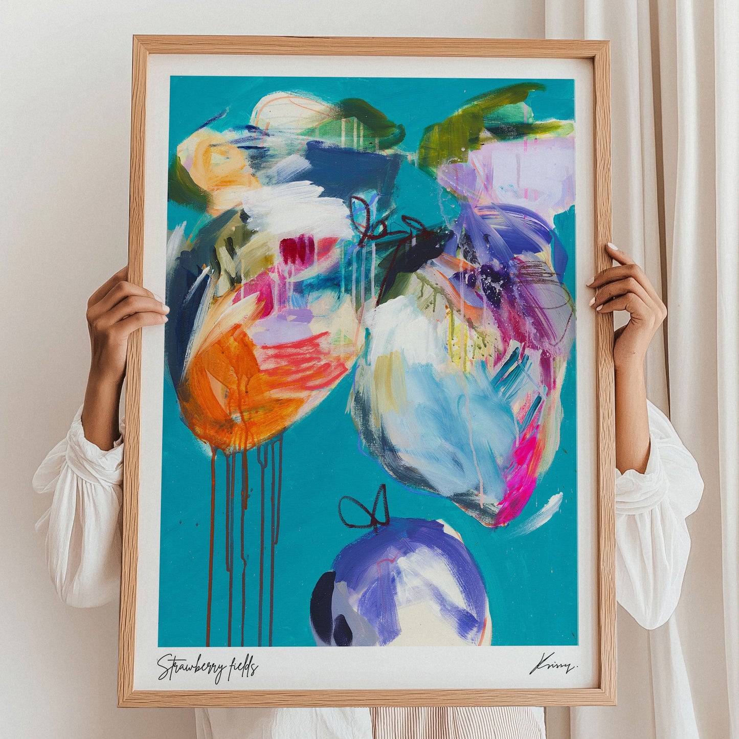 Person holding a colorful abstract painting in a wooden frame against a white wall.