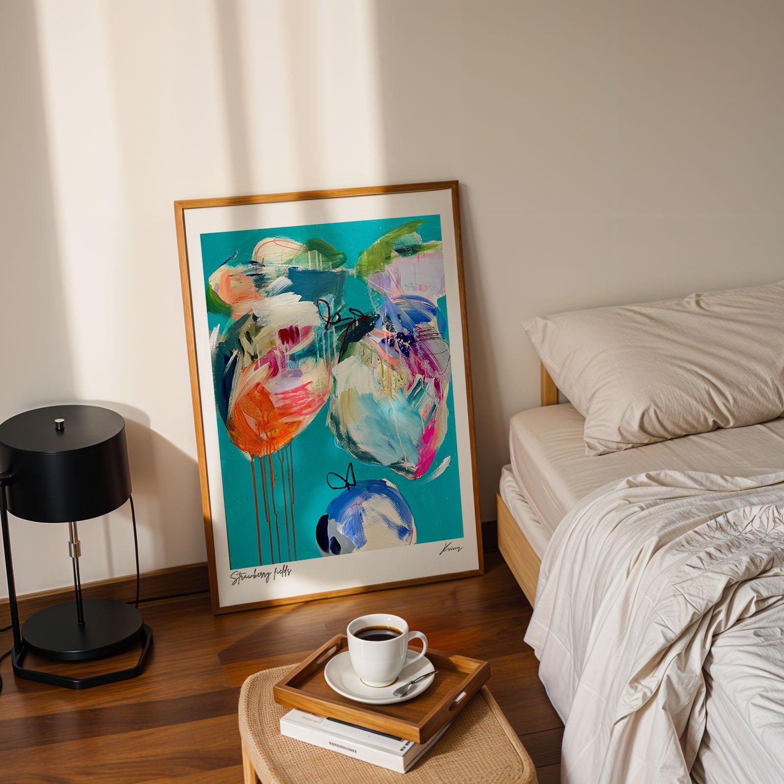 Colorful abstract painting on a wall next to a bed with a lamp and coffee cup on a side table.