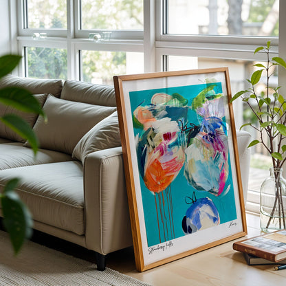 Framed abstract art on a table in a living room with a couch and plants.