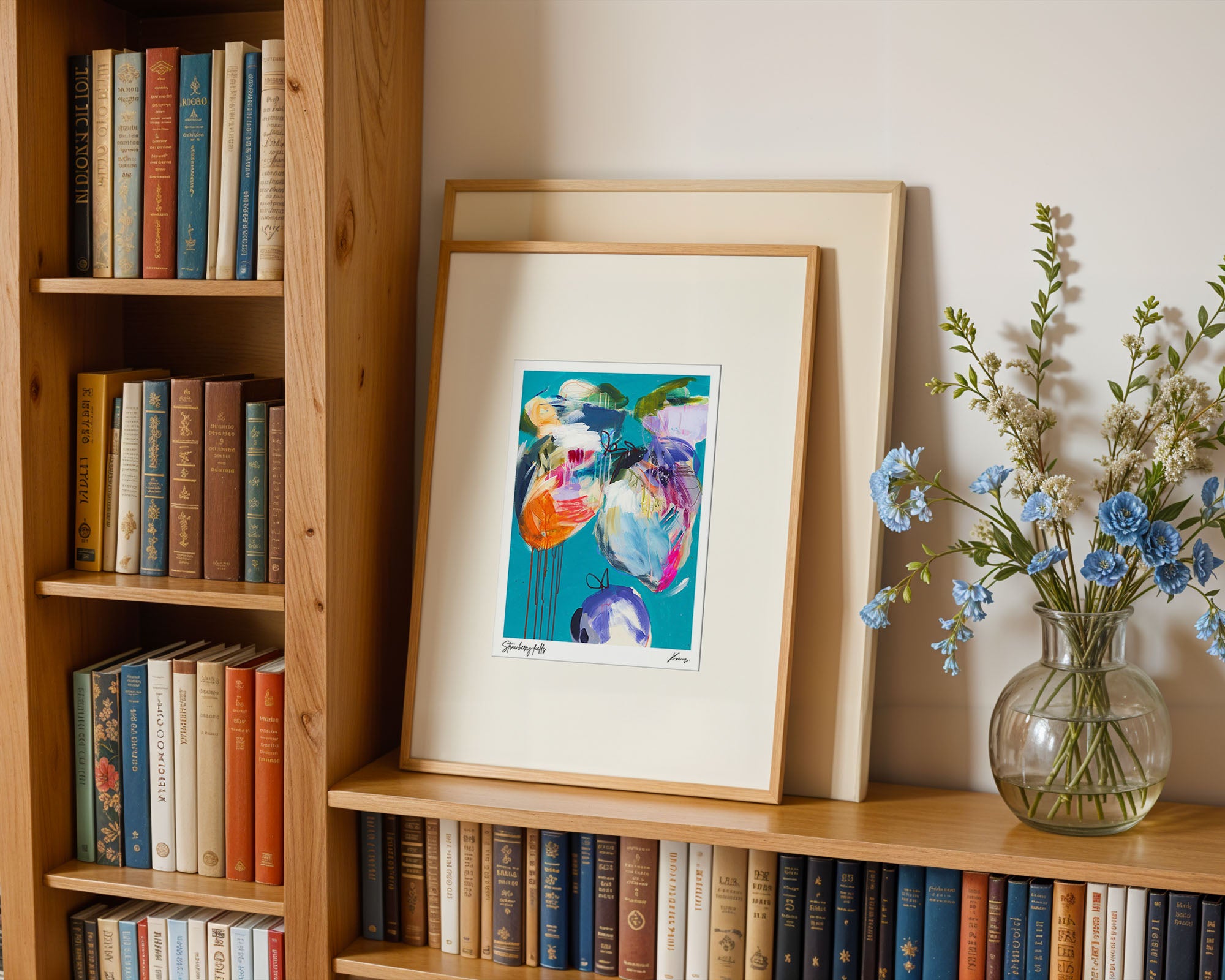 Framed artwork on a bookshelf with books and a vase of flowers.
