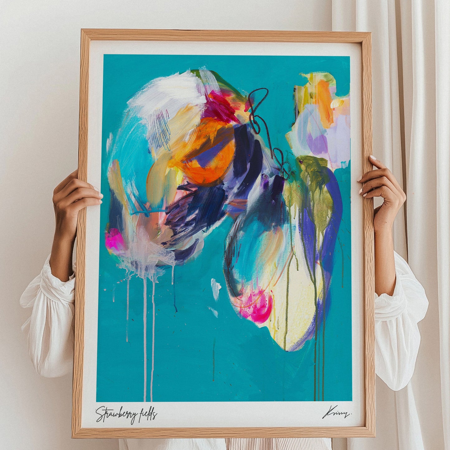 Person holding a colorful abstract painting in a wooden frame against a white wall.