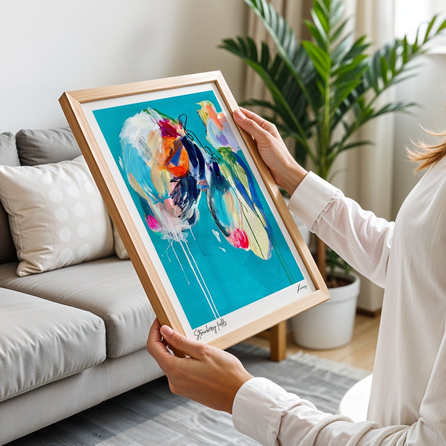 Person holding a framed abstract painting in a living room