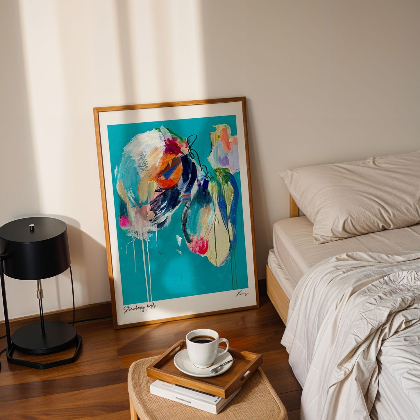 Colorful abstract painting on a wall next to a bed with a lamp and coffee cup on a side table.