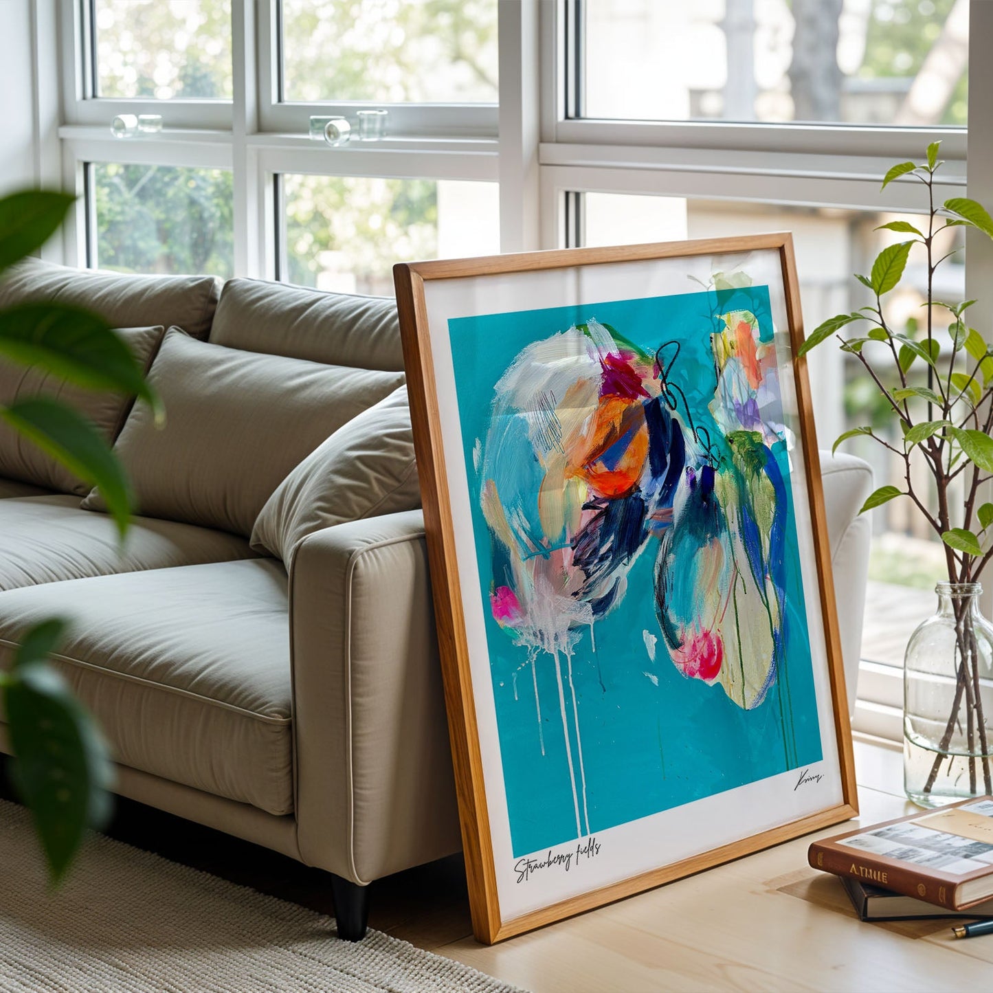 Framed abstract art on a table in a living room with a couch and plants.