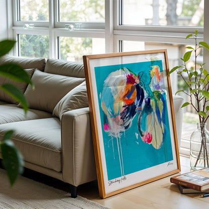 Framed abstract art on a table in a living room with a couch and plants.