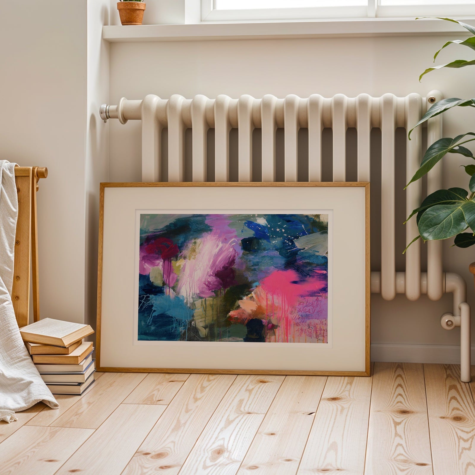 Framed abstract painting on a wooden floor with a radiator and plant in the background