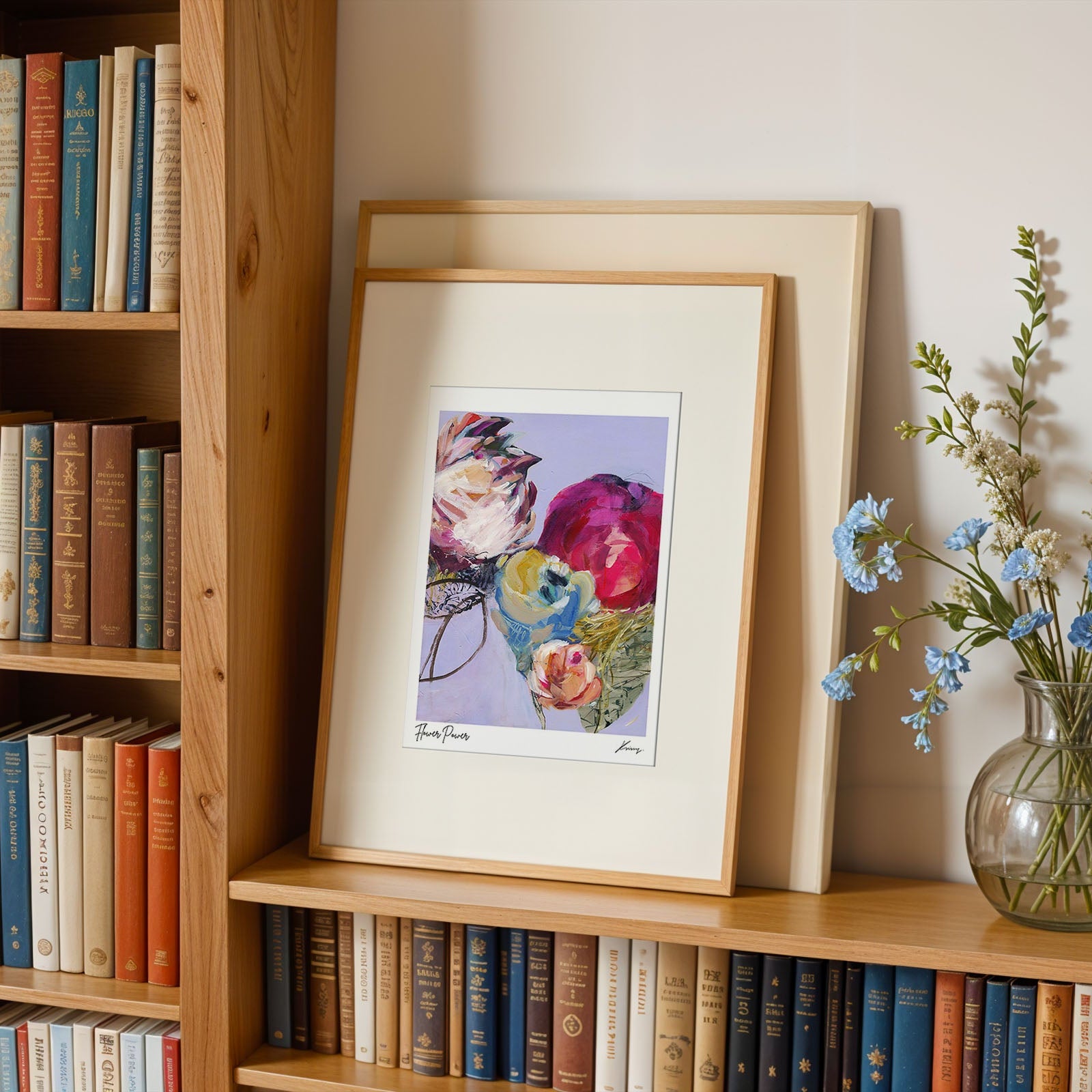 Framed floral print on a bookshelf with books and a vase of flowers.