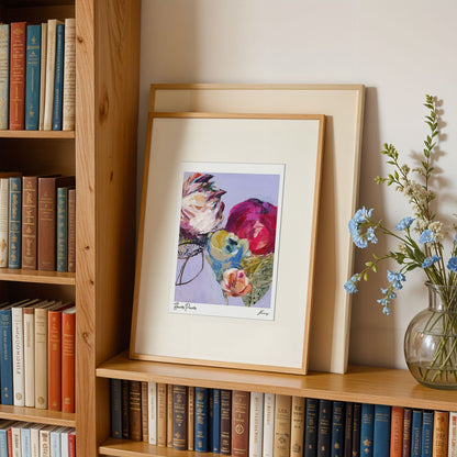 Framed floral print on a bookshelf with books and a vase of flowers.
