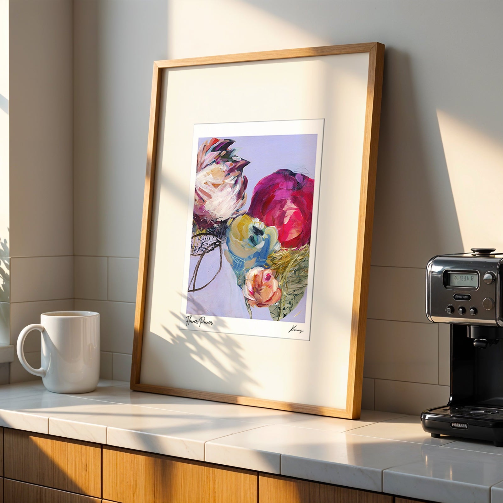 Framed floral artwork on a kitchen counter with a coffee machine and mug.