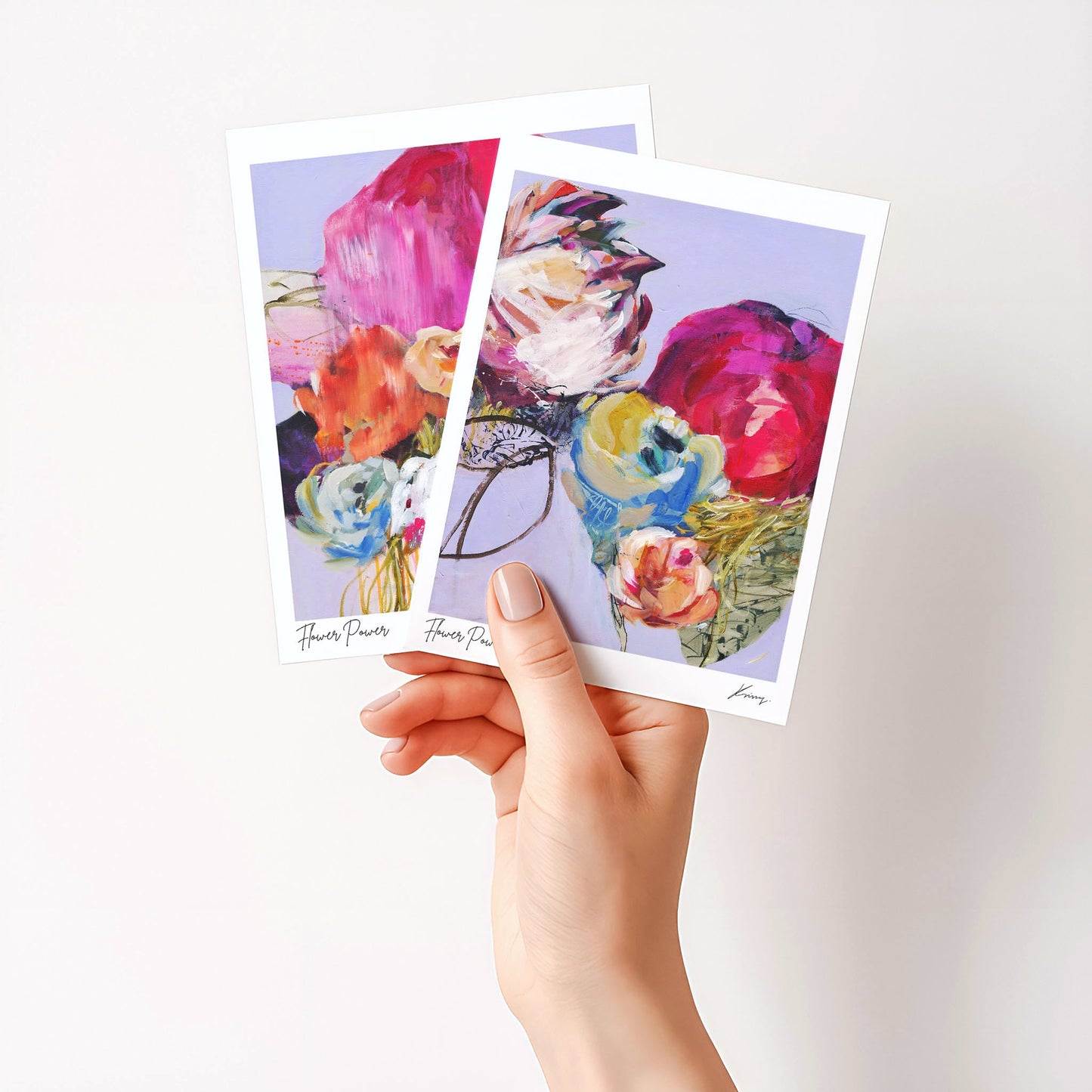 Hand holding two floral postcards with a white background