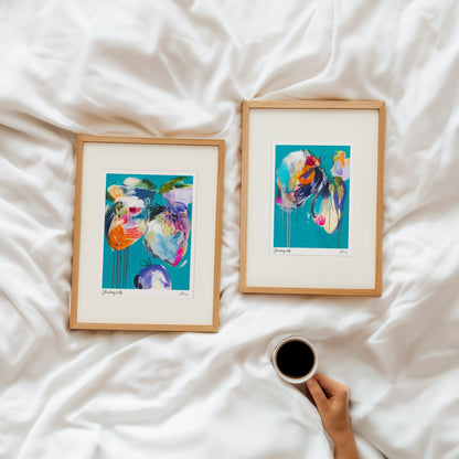 Two framed abstract artworks on a white bed with a hand holding a coffee cup.