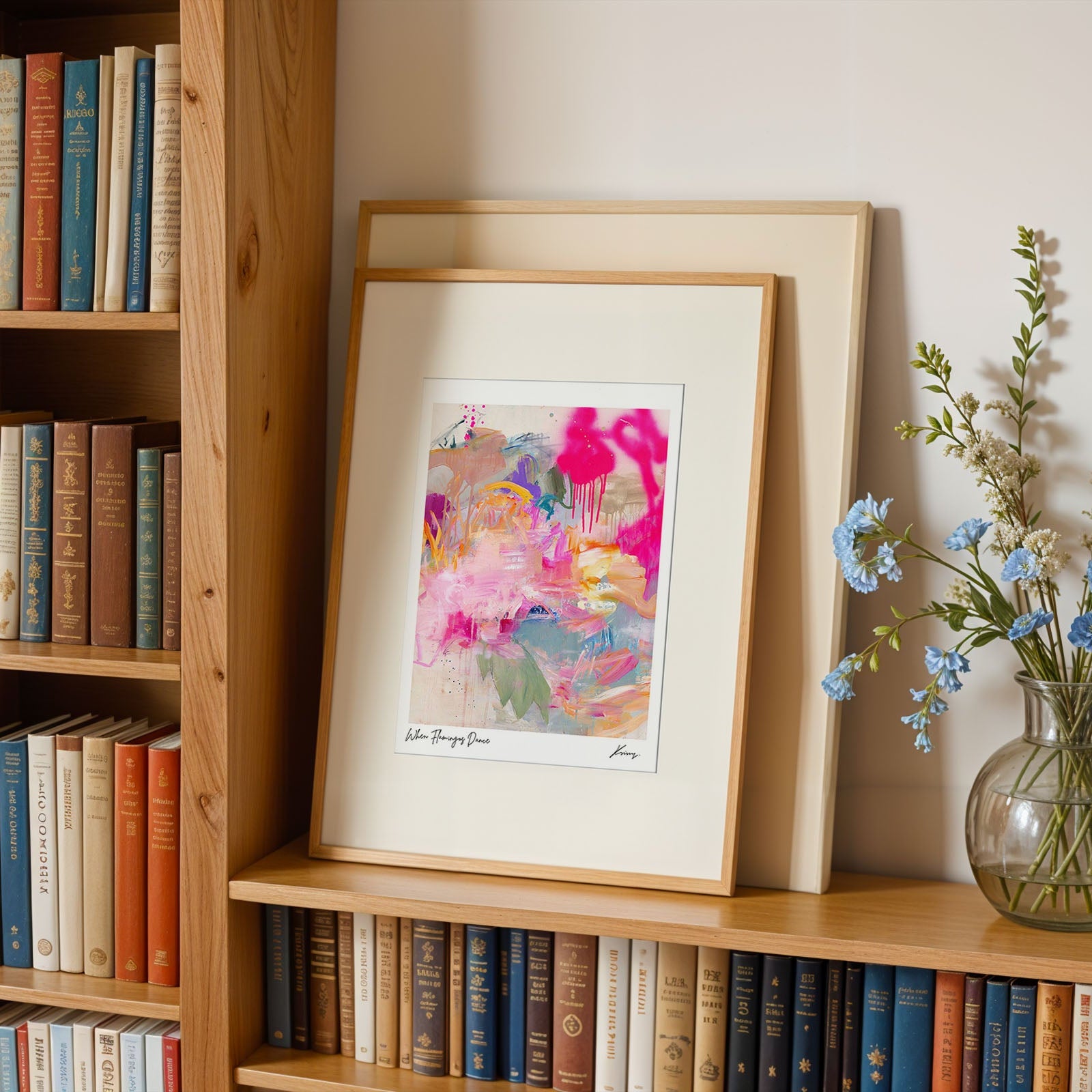 Framed abstract art on a bookshelf with books and a vase of flowers.
