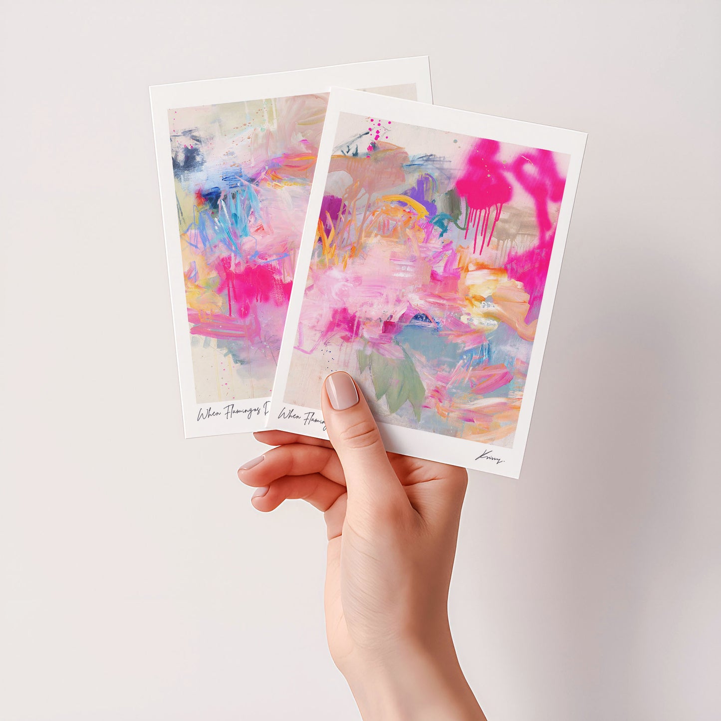 Two abstract art prints held by a hand against a light background