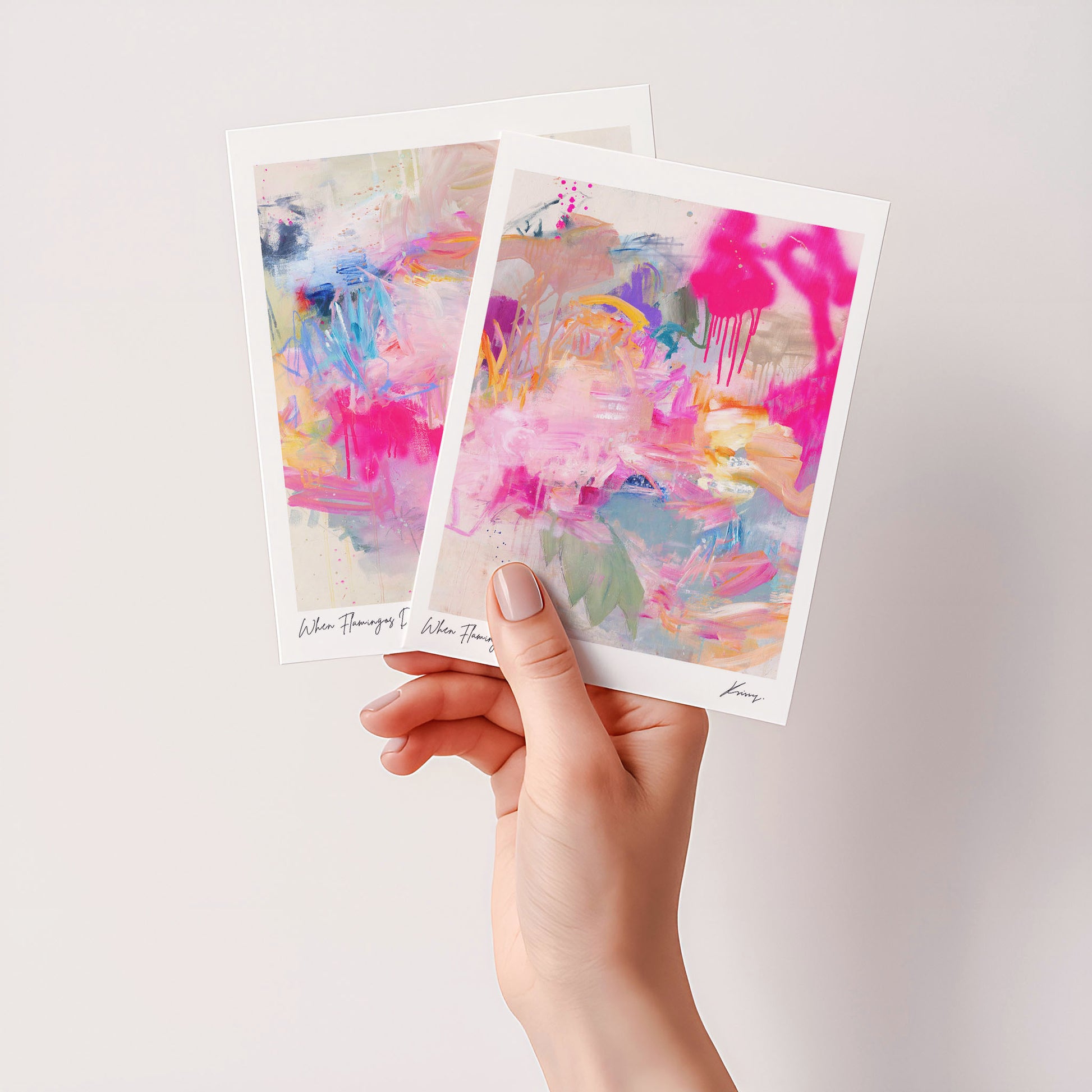 Two abstract art prints held by a hand against a light background