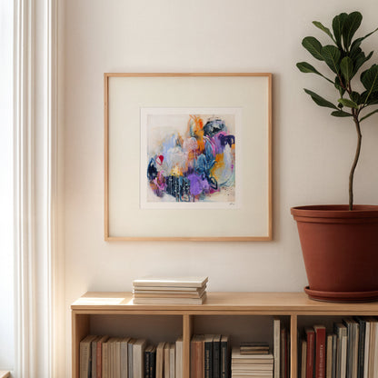 Framed abstract artwork on a wall above a bookshelf with books and a plant.