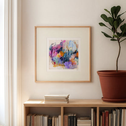 Framed abstract art on a wall above a bookshelf with books and a plant.
