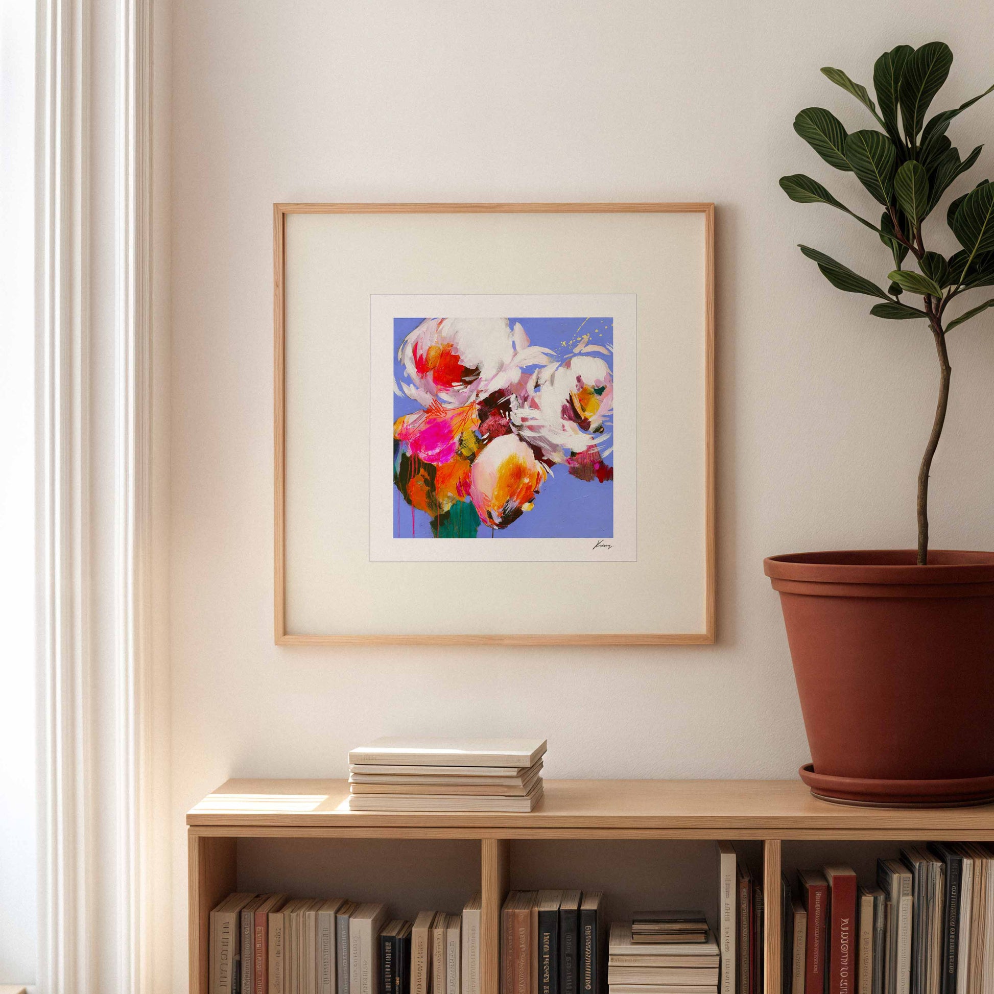 Framed abstract artwork on a wall above a bookshelf with books and a plant.