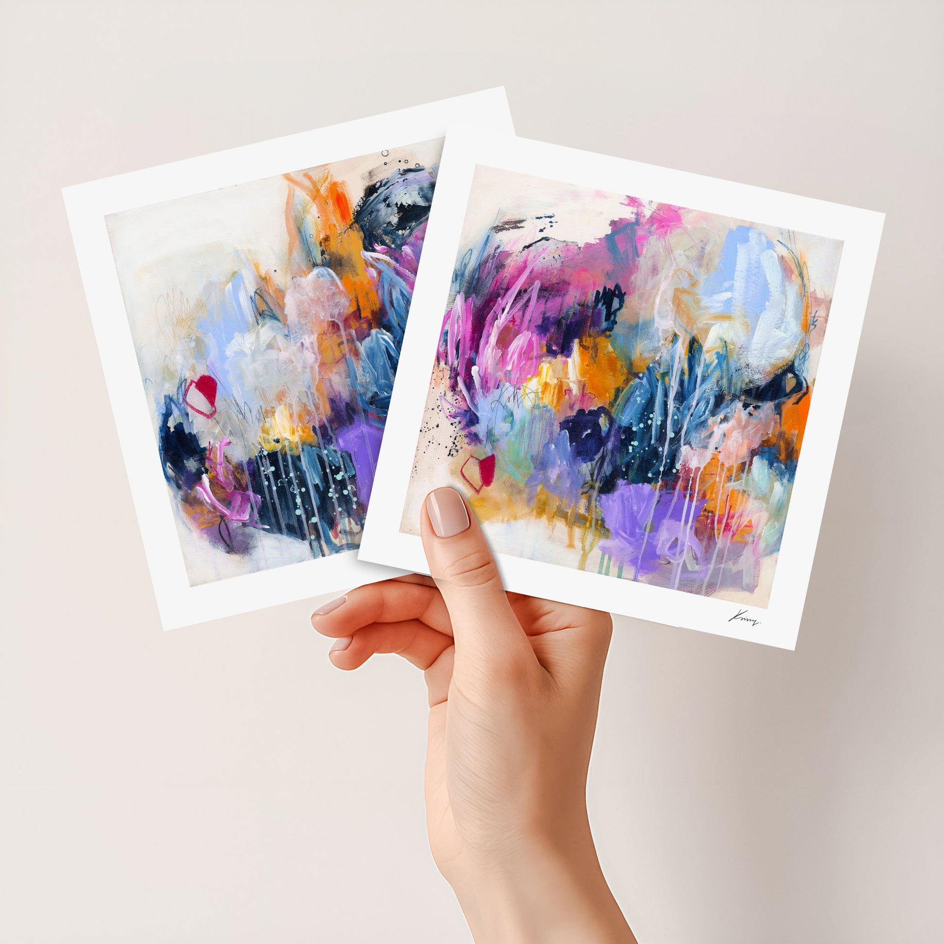 Two abstract art prints held by a hand against a light background