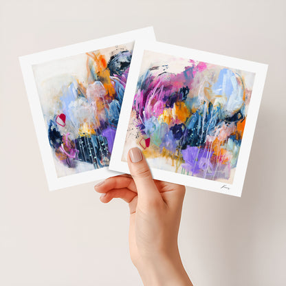 Two abstract art prints held by a hand against a light background