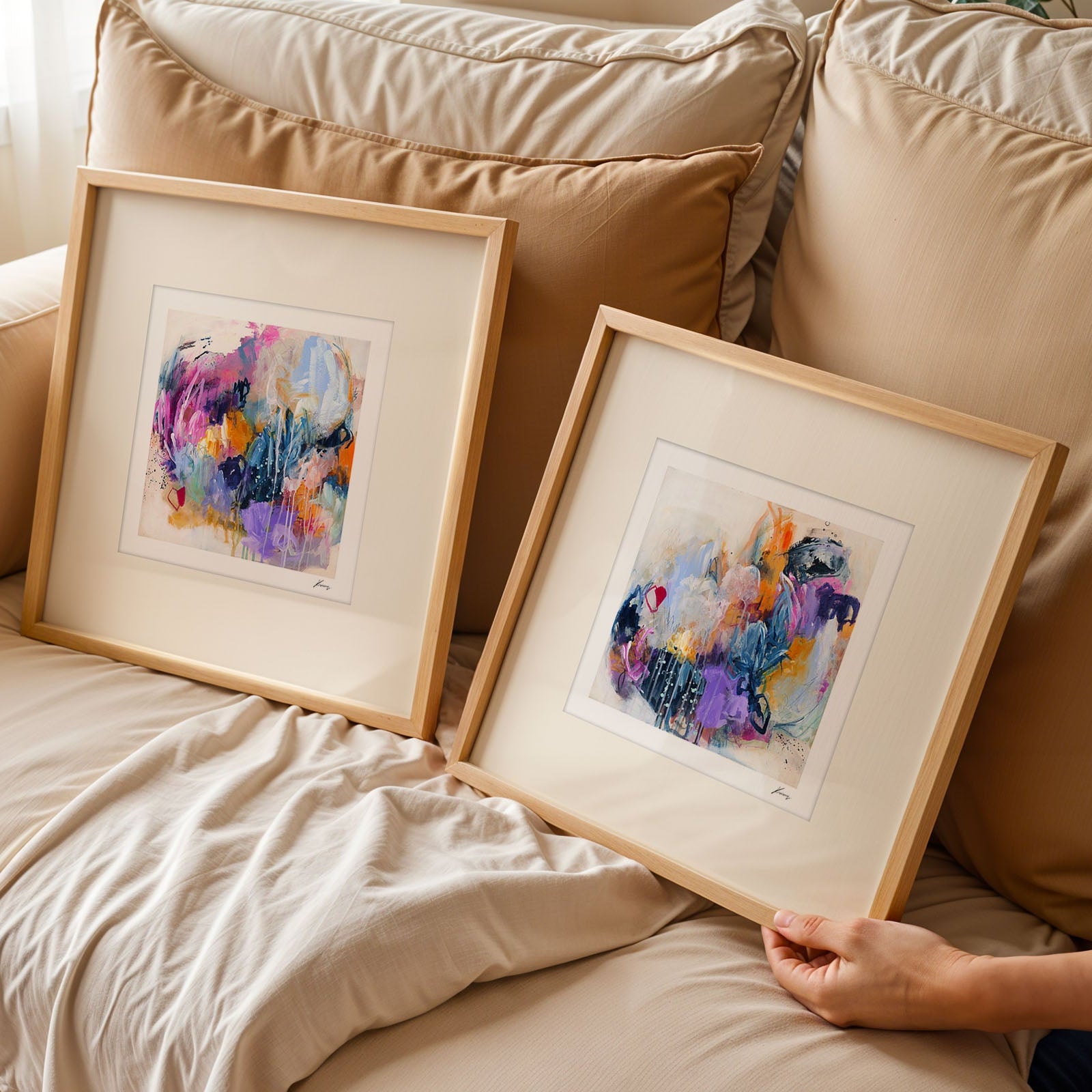 Two framed pieces of abstract art on a beige sofa.