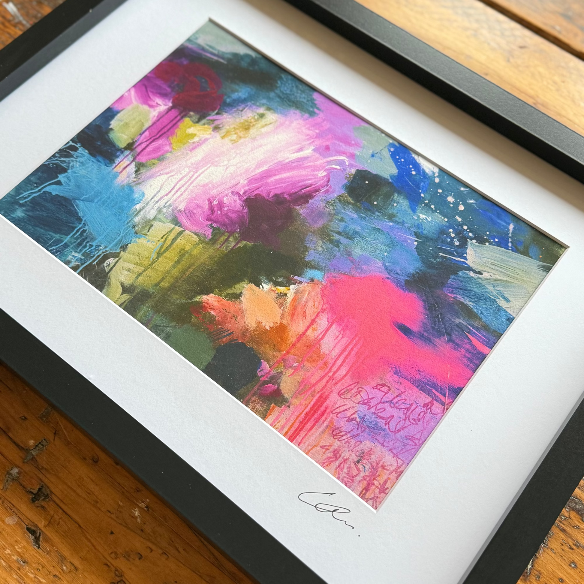 Framed abstract painting with vibrant colors on a wooden surface