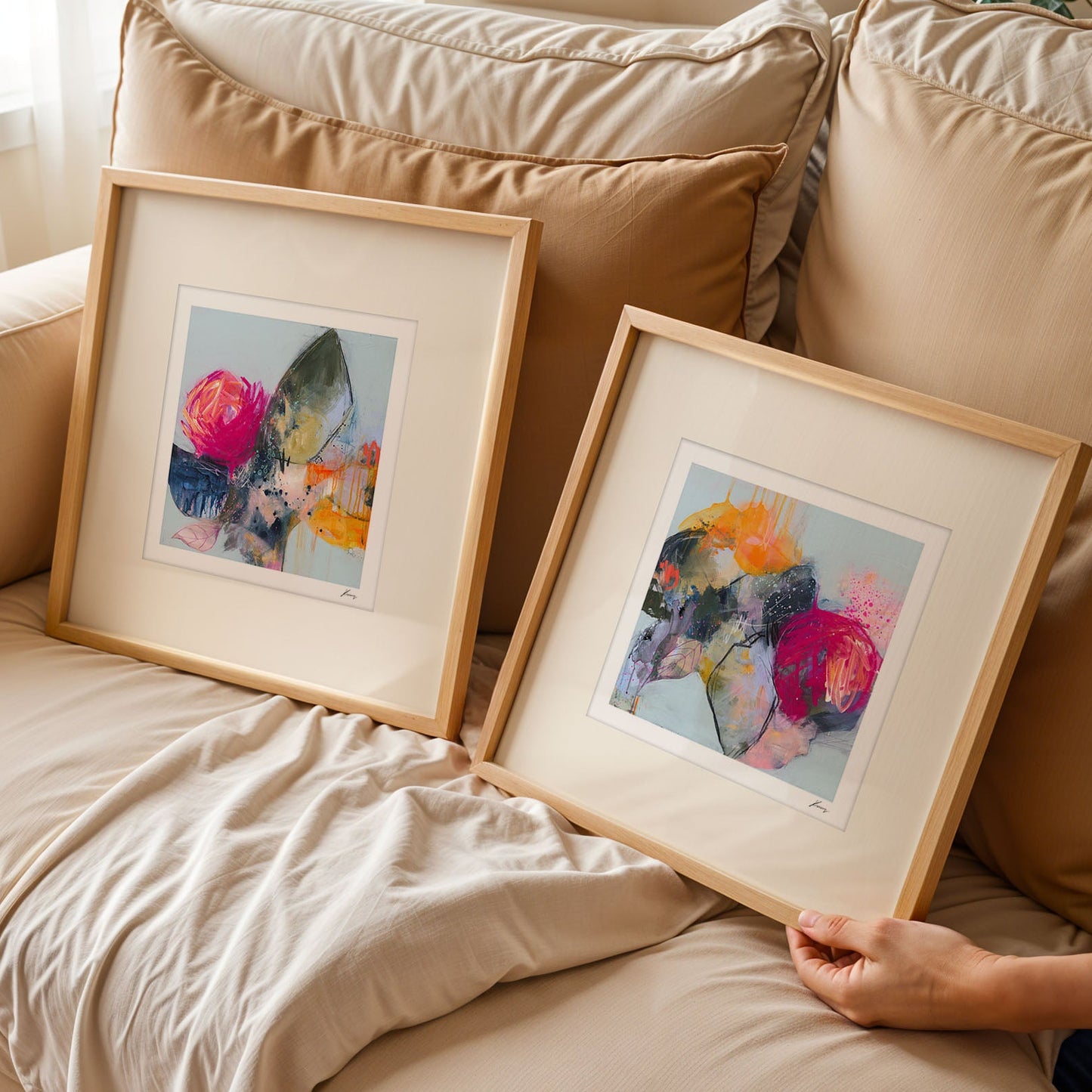 Two framed pieces of abstract art on a beige couch.
